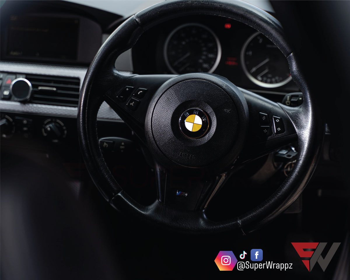 Half Yellow Carbon BMW badge overlay on a steering wheel badge, close-up