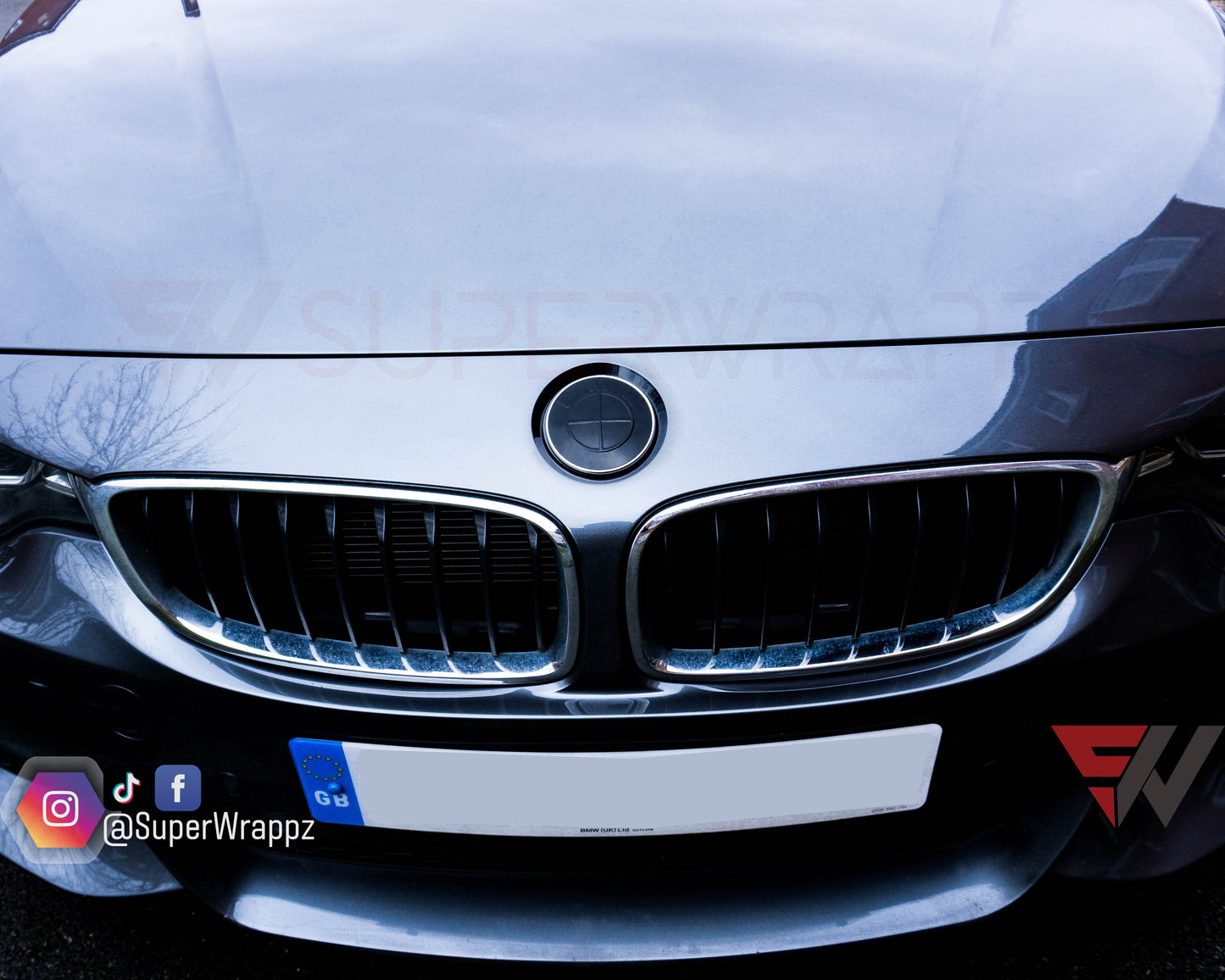 Black Gloss 2-Piece BMW badge tint overlay on the front hood badge, close-up