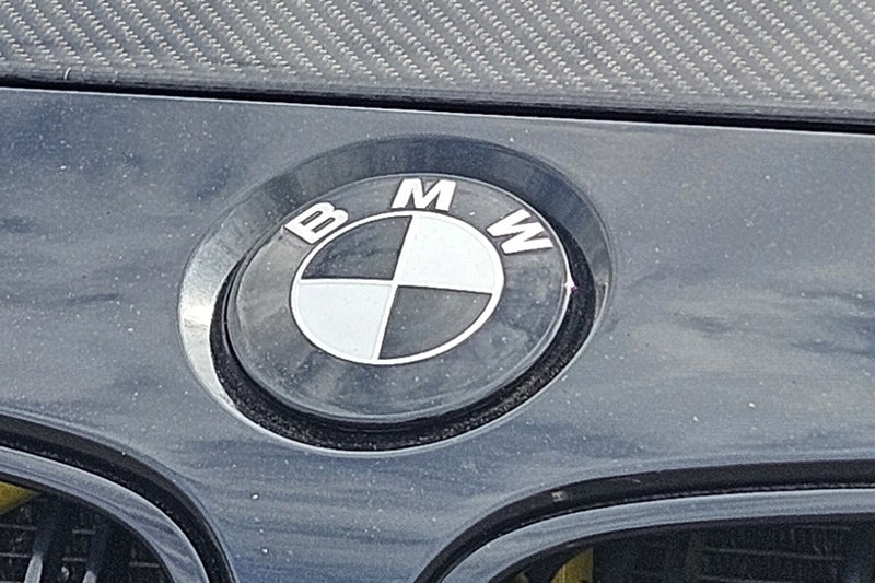 Dark BMW F80 M3 bonnet with carbon strip, wearing a SuperWrappz blacked-out badge overlay. Compatible with BMW &mdash; Not Genuine BMW Parts.