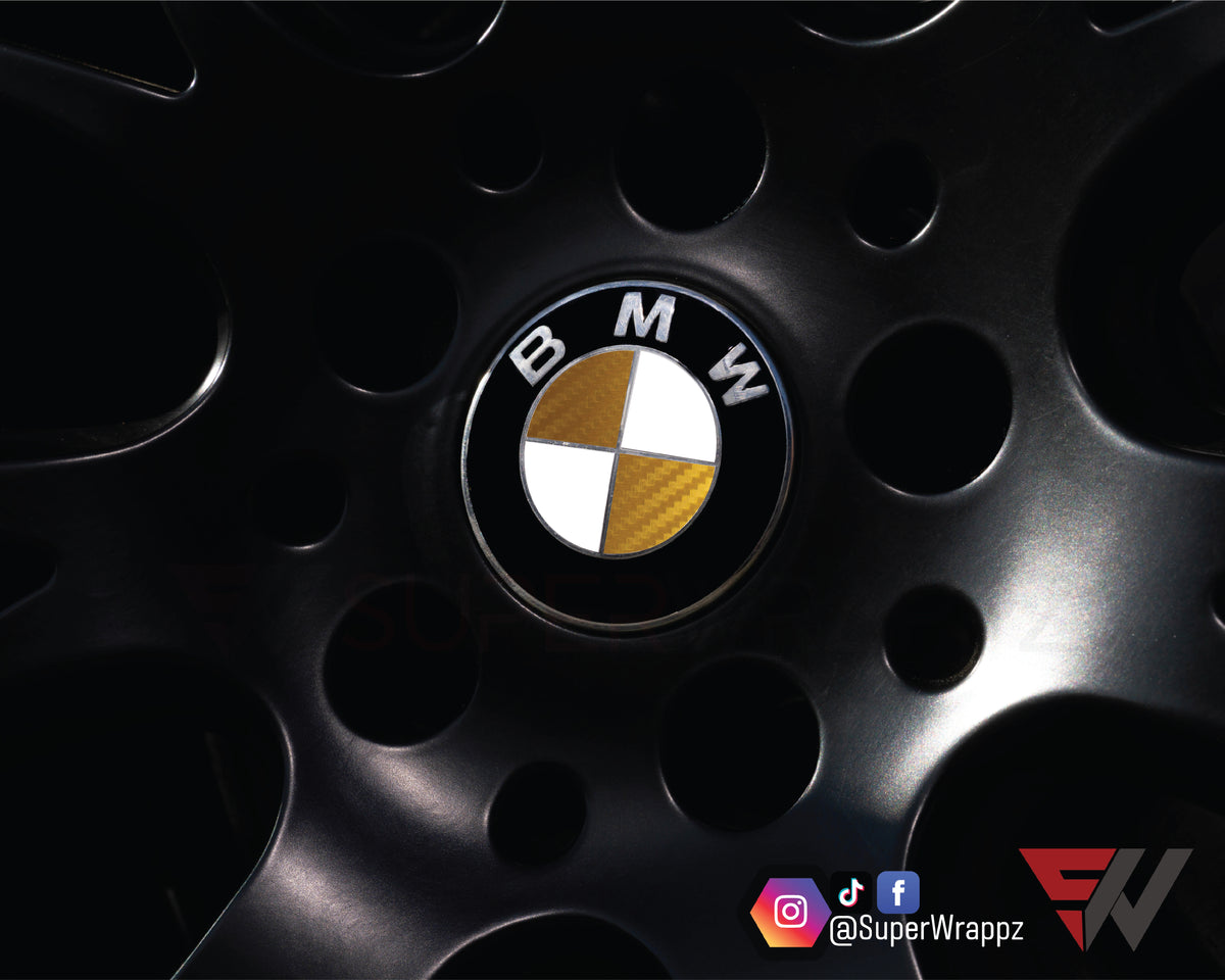 Half Gold Carbon BMW badge overlay on an alloy wheel centre cap, close-up
