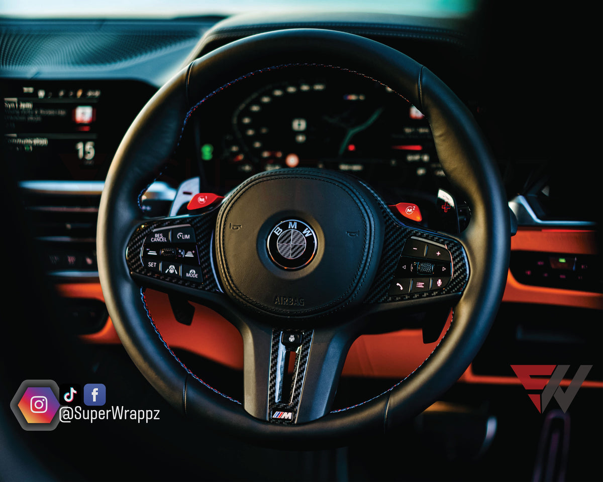 Black & Dark Grey Carbon V2 BMW badge overlay on a steering wheel badge, close-up