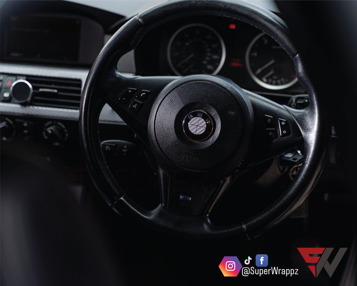Full Silver Carbon BMW badge overlay applied to a steering wheel centre badge, close-up