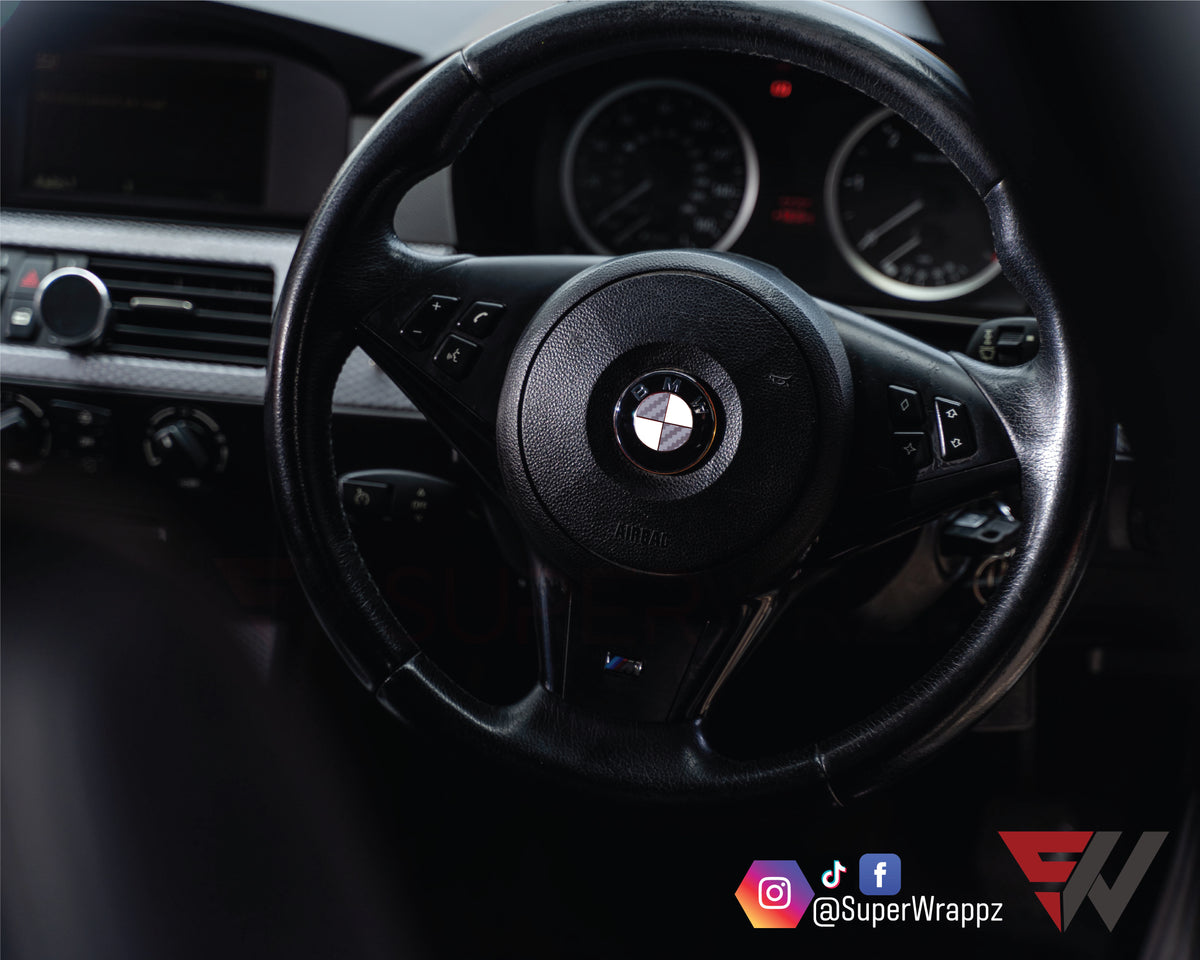 Half Silver Carbon BMW badge overlay on a steering wheel badge, close-up