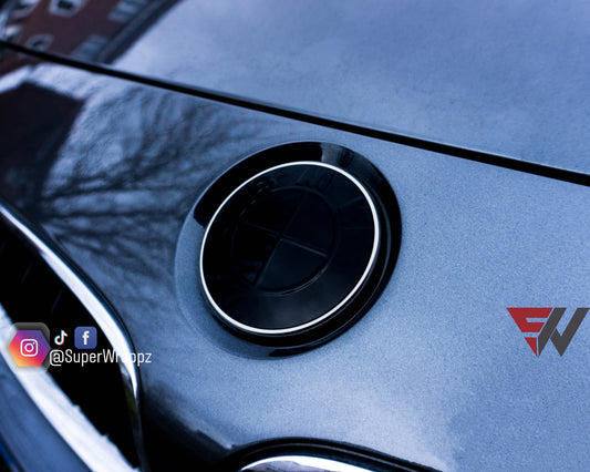 Black gloss 2-piece BMW badge tint overlay by SuperWrappz on E/F Series emblems, aftermarket vinyl